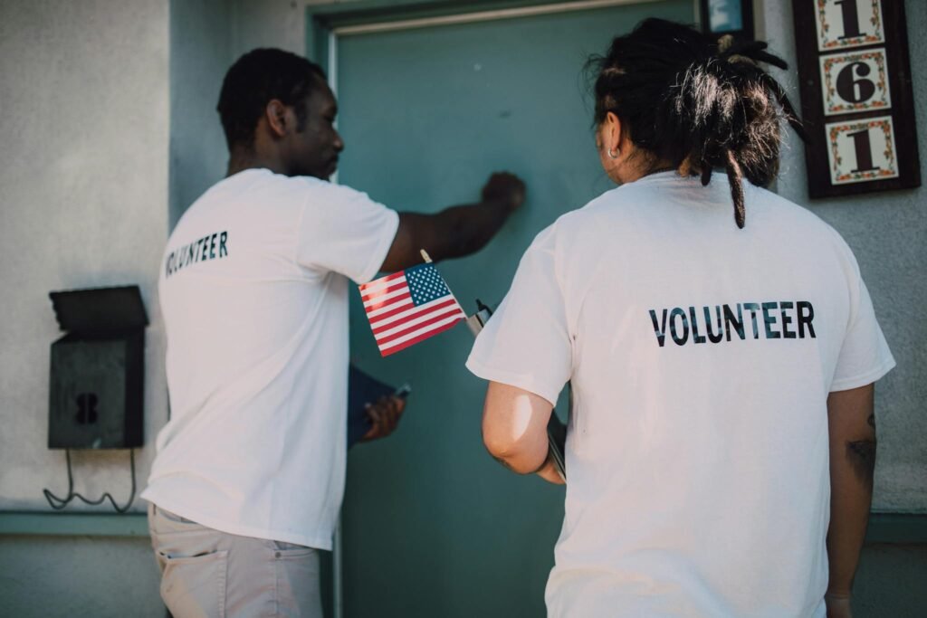 Two volunteers knocking on door during a community outreach event, holding a small American flag.